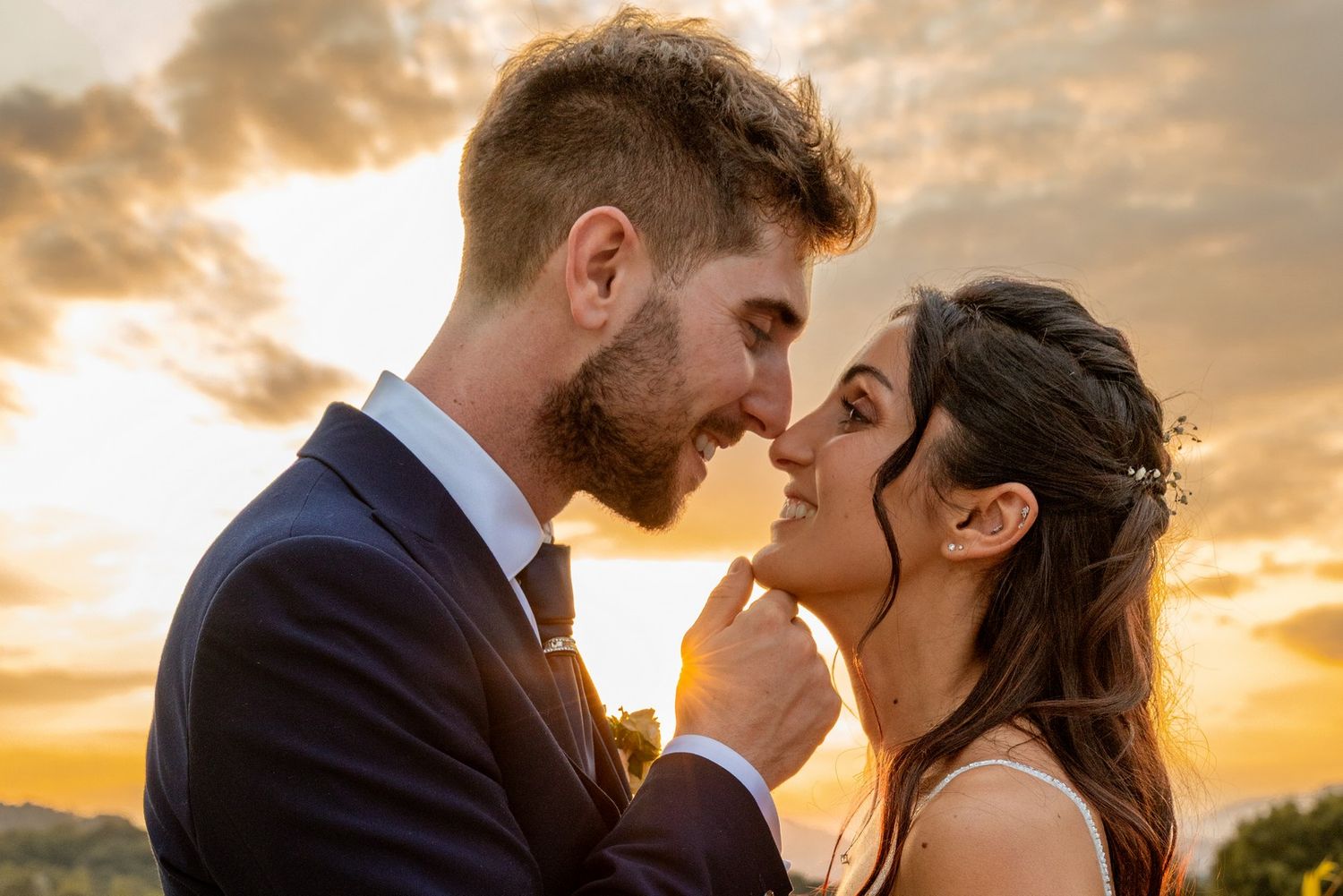 Intimate wedding couple embracing during golden hour with dramatic sunset clouds.
