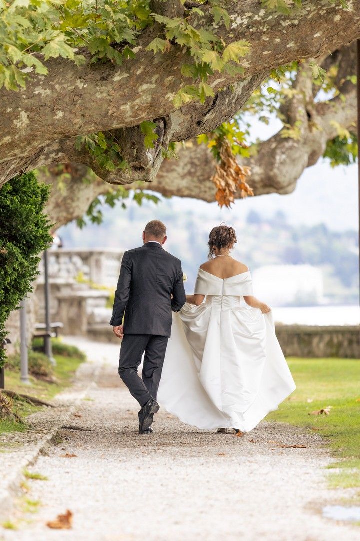 A couple walking down a tree-lined garden path on their wedding day, with the bride in a flowing white gown.