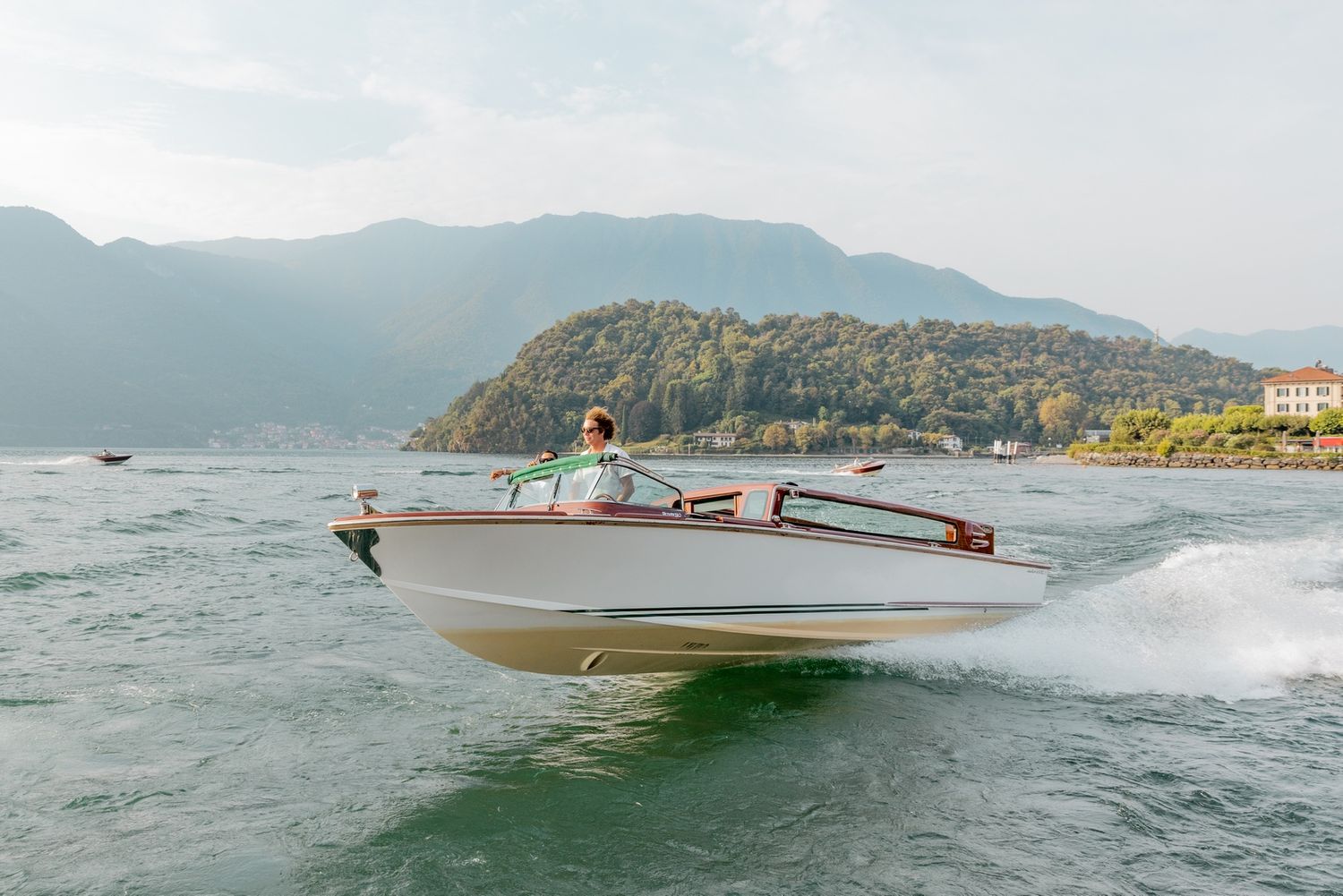 Vintage speedboats create white wakes while racing across a scenic mountain lake.