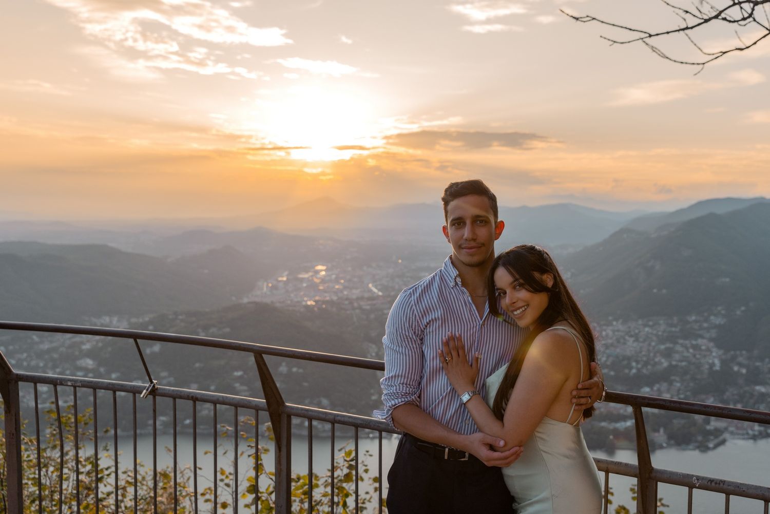 A couple embraces while watching sunset over mountain landscape from scenic overlook viewpoint.