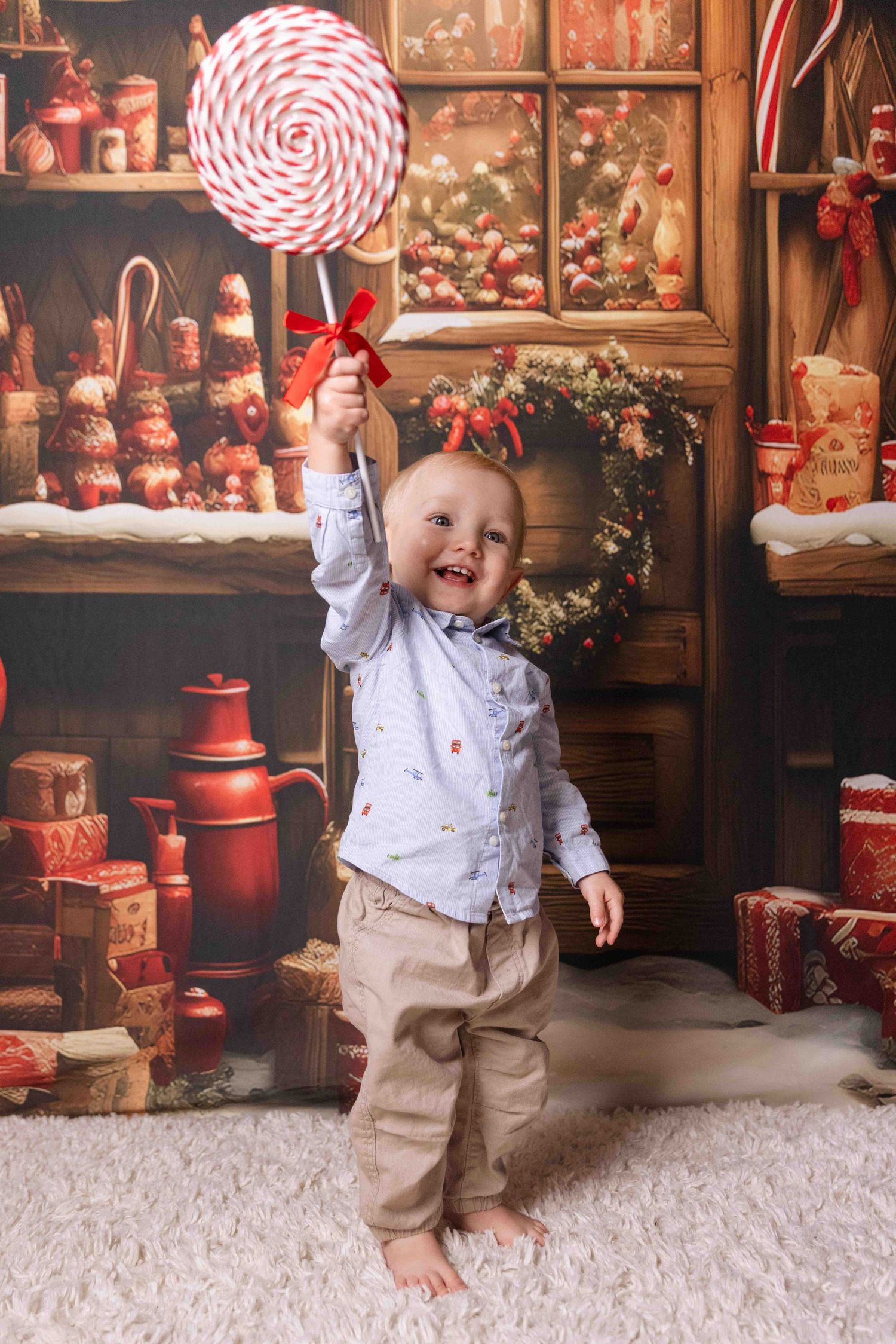 Toddler in white outfit playing with giant candy cane props against holiday backdrop.