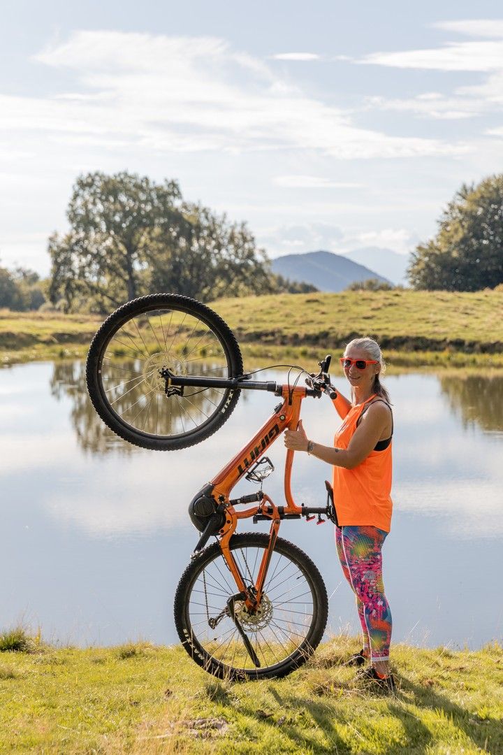 Sequence of someone lifting an orange mountain bike by a scenic lake.