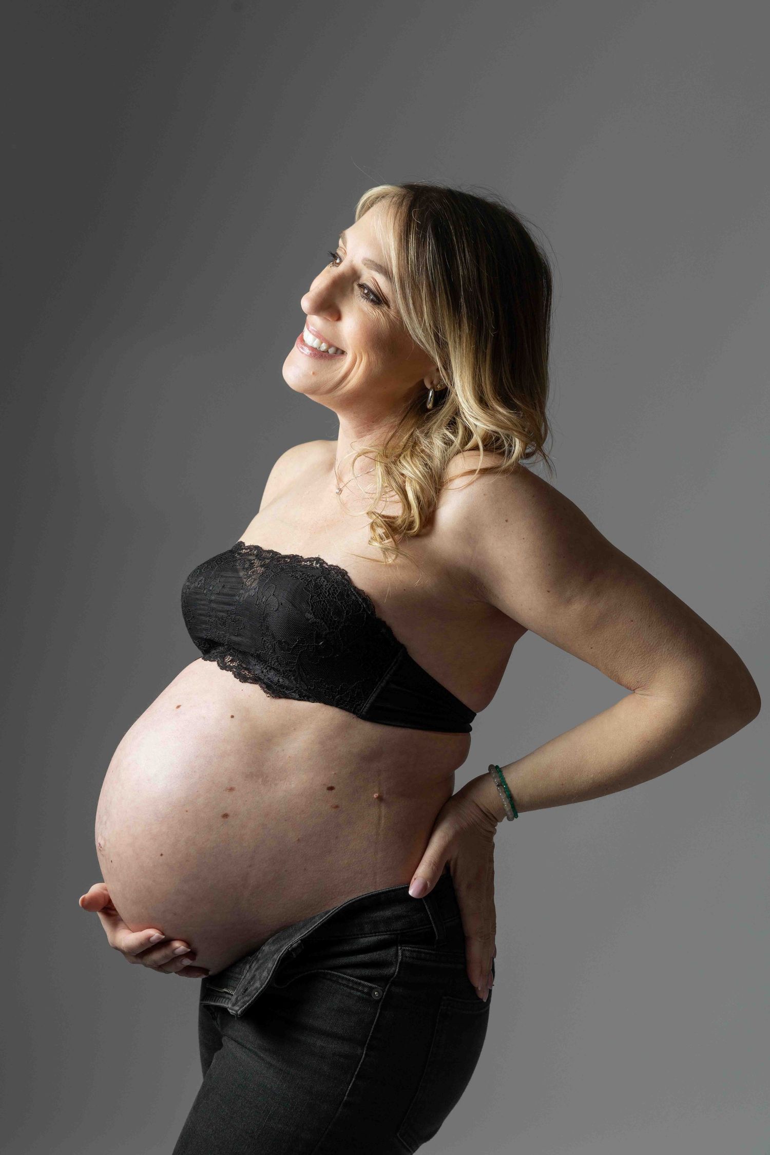 Artistic maternity photos in black and white showing a pregnant woman in a black top against grey background.