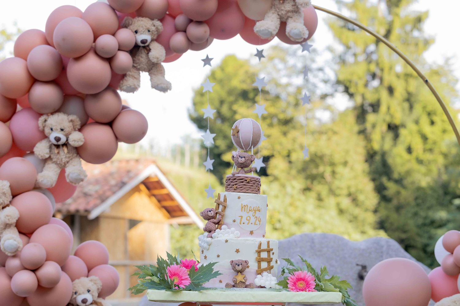 Pink balloon arch decorates elegant party setup with whimsical cake centerpiece.