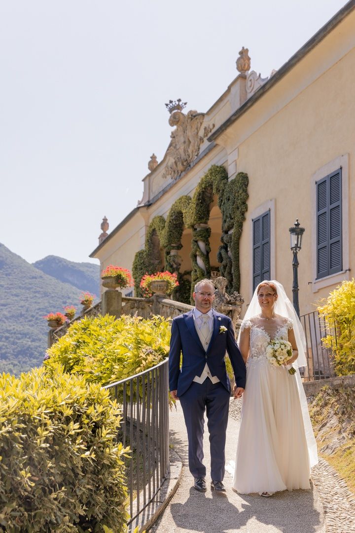 Newlyweds walking along a Mediterranean villa pathway with mountain views.
