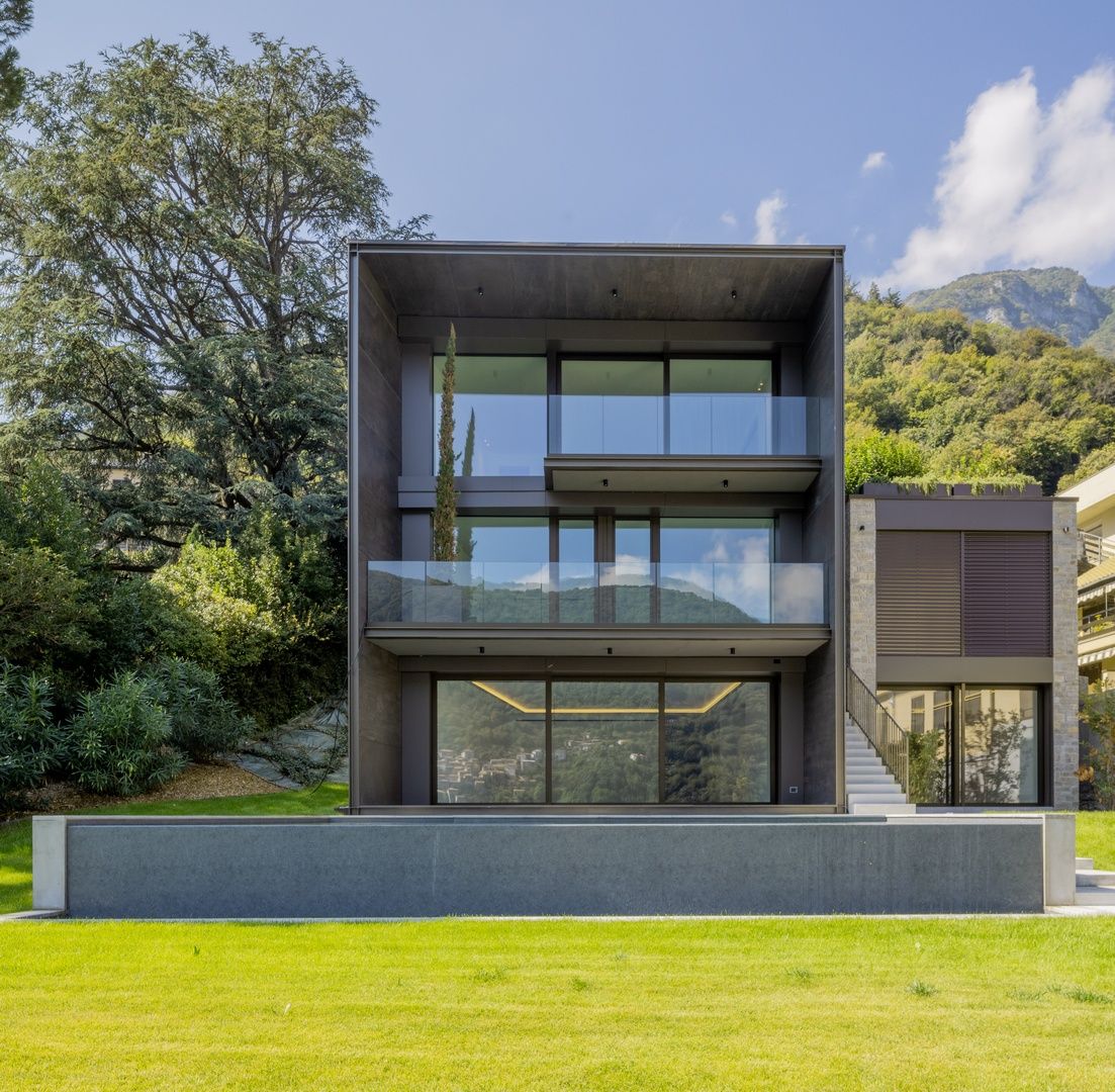 A modern minimalist black house with large glass windows sits on a green lawn under blue skies.