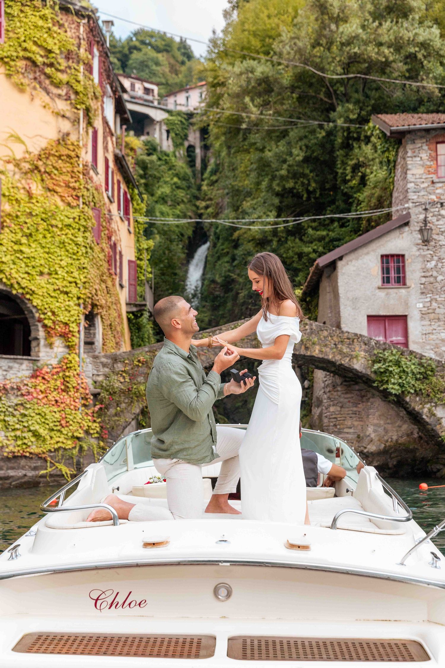 A couple shares a romantic moment on a boat named Chloe with ivy-covered buildings in the background on Lake Como.