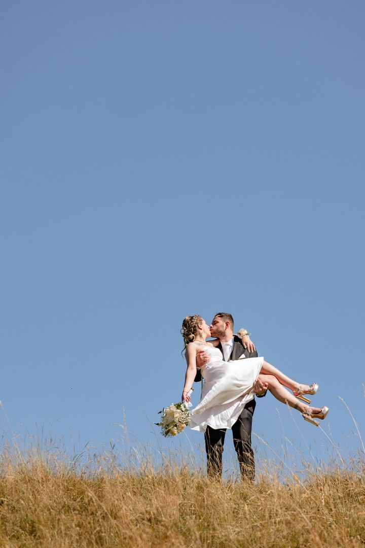 Romantic dip pose silhouetted against blue sky on hilltop meadow.