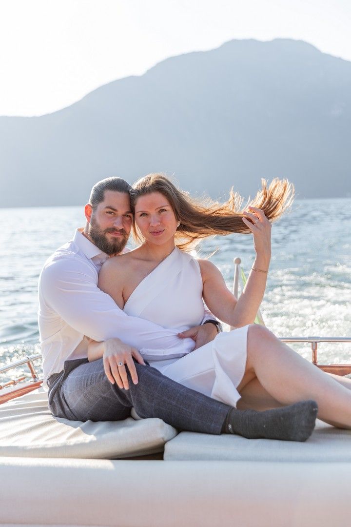 Relaxed couple lounging on a boat deck with mountains and sparkling water in the distance.