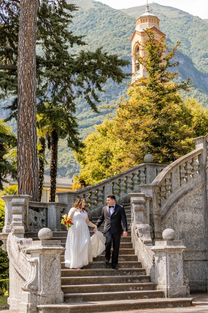 Wedding couple descending ornate stone steps with mountains and architecture in the background.