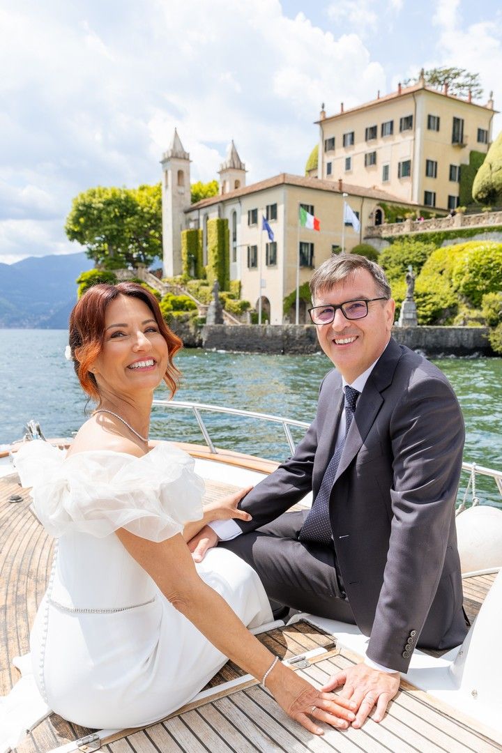 Wedding couple enjoys a romantic moment on a boat deck with Italian lakeside architecture in background.