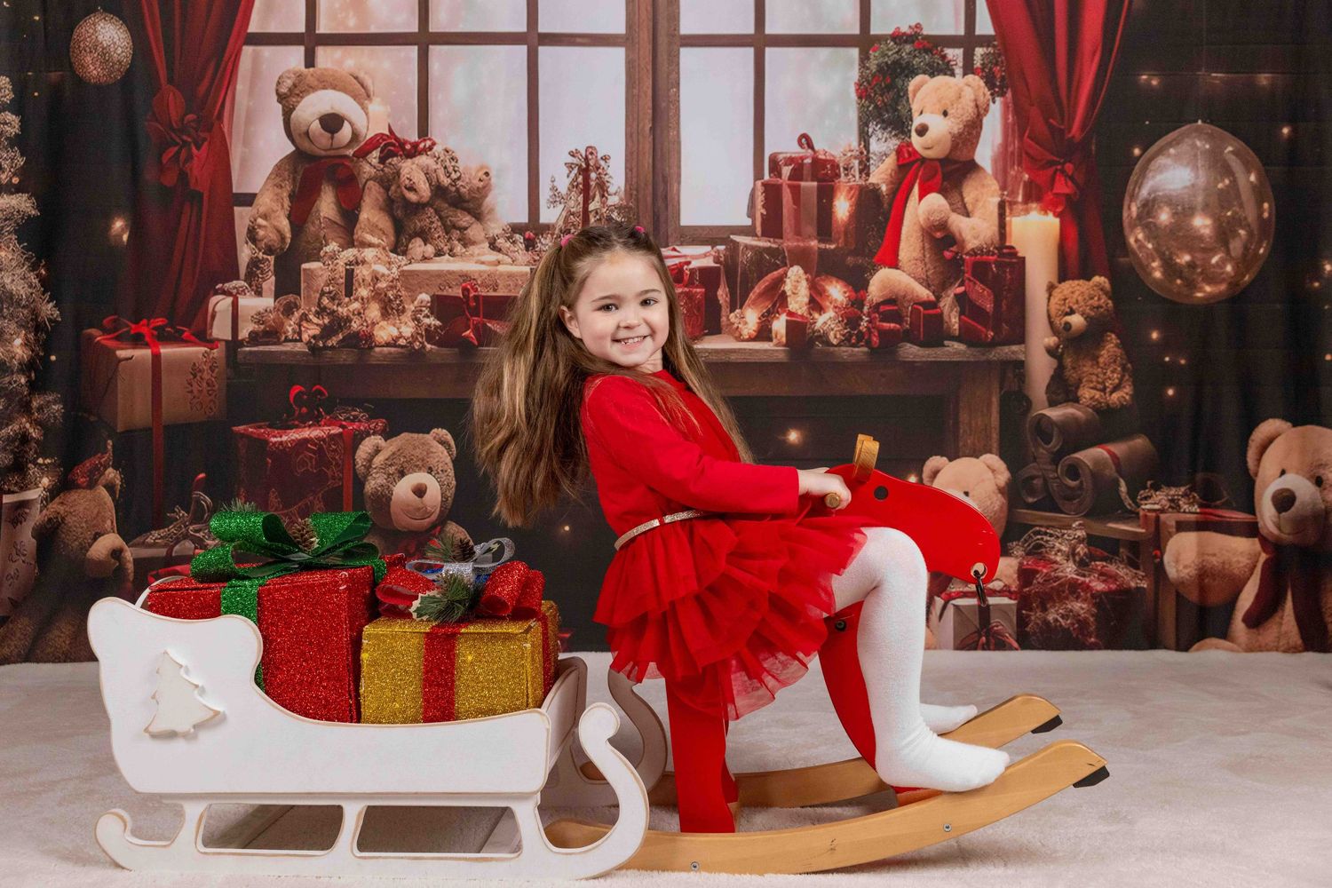 Christmas photo setup with white sleigh prop and wrapped presents against dark backdrop.
