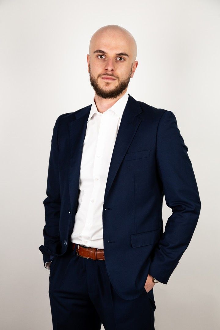 Professional in navy suit and white shirt standing against white background.