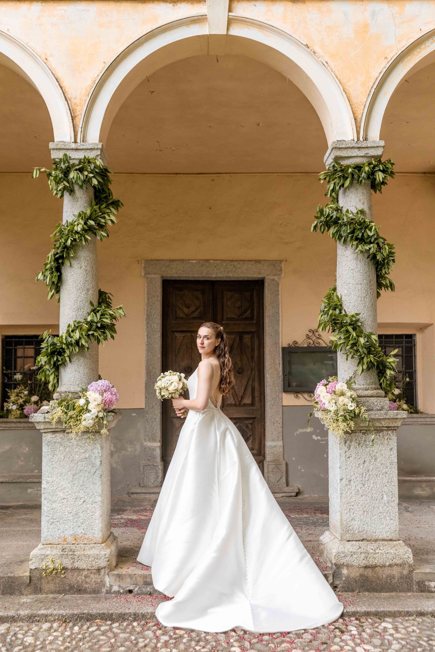 White wedding gown displayed in multiple angles under a Mediterranean style portico with climbing vines.