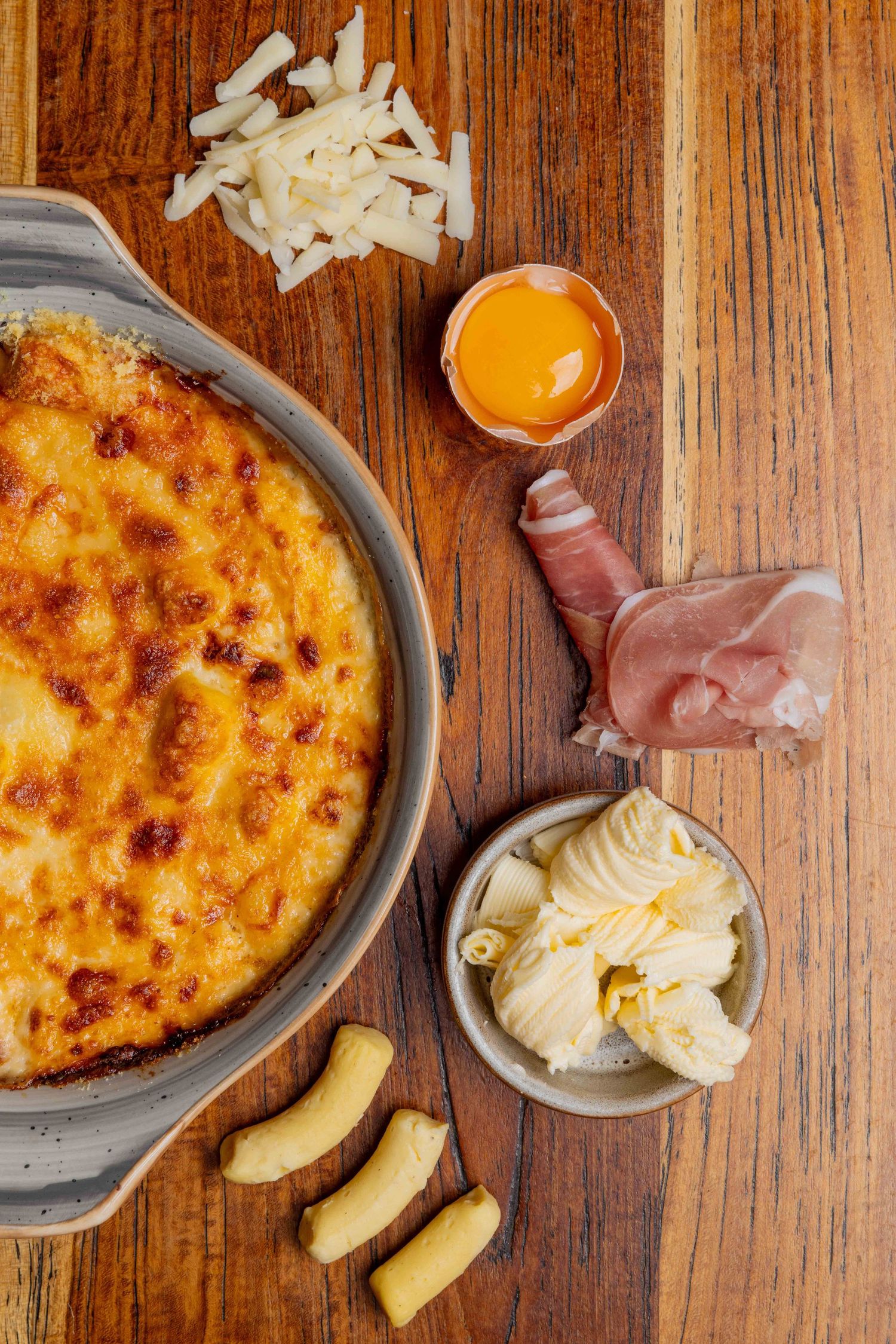 Artisanal cheese plate with prosciutto and melted cheese displayed on a rustic wooden table.