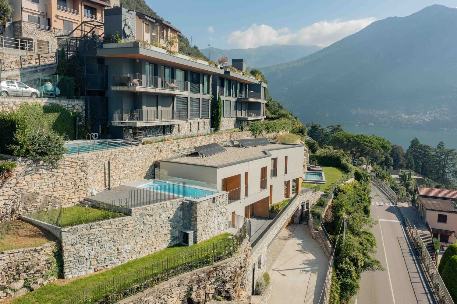 Aerial view of luxury hillside properties with stone walls and swimming pools overlooking mountains.