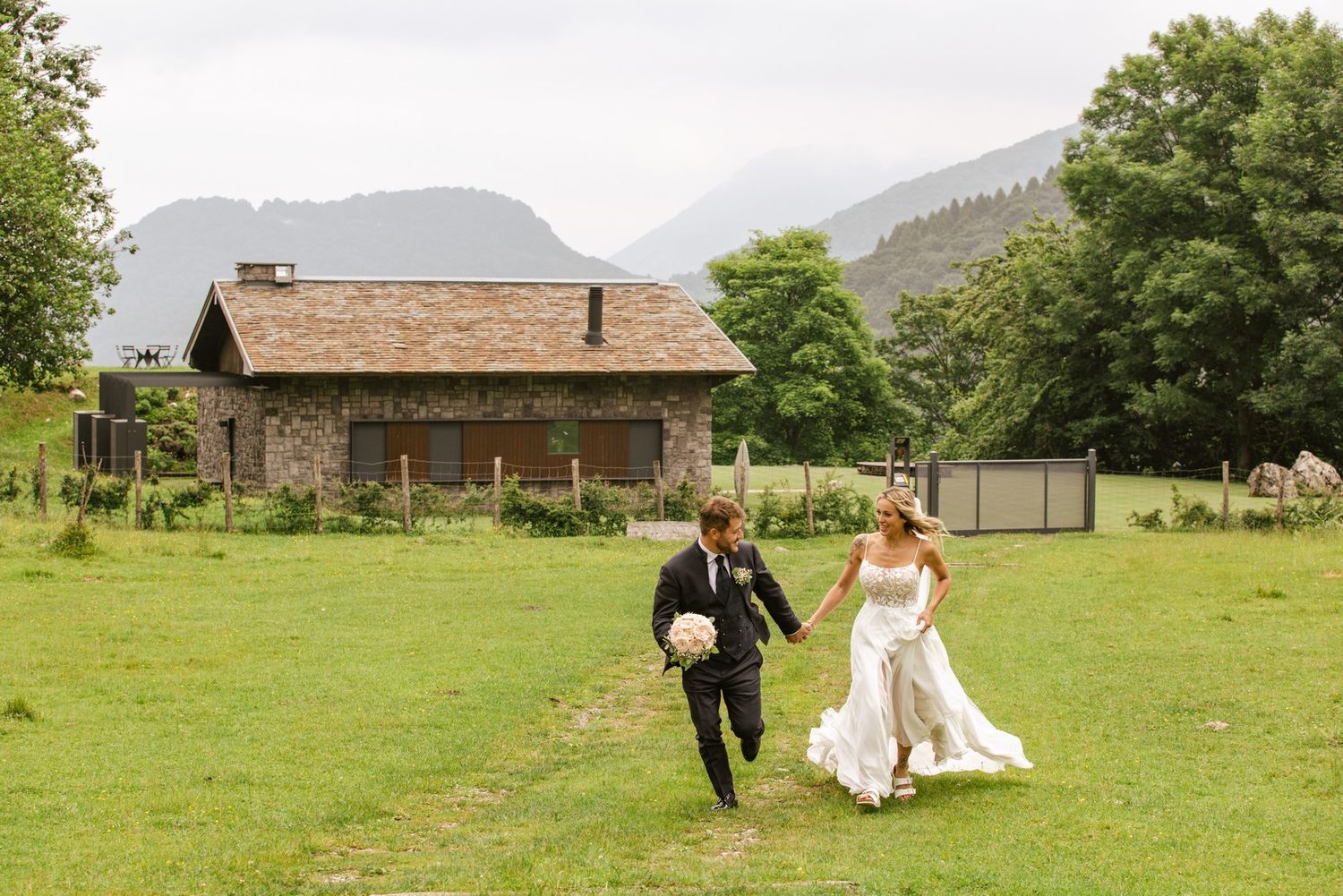Wedding couple walking through a lush green field with mountains in the background.