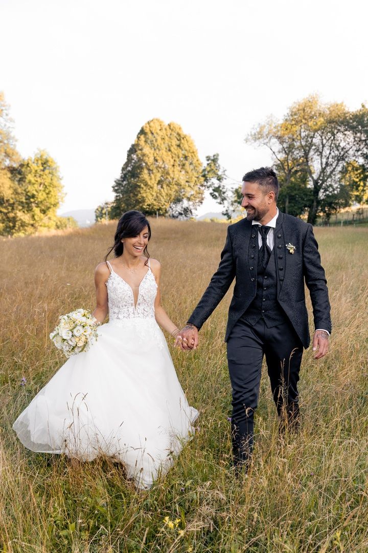 Bride and groom walking through tall grass field holding hands during sunset.