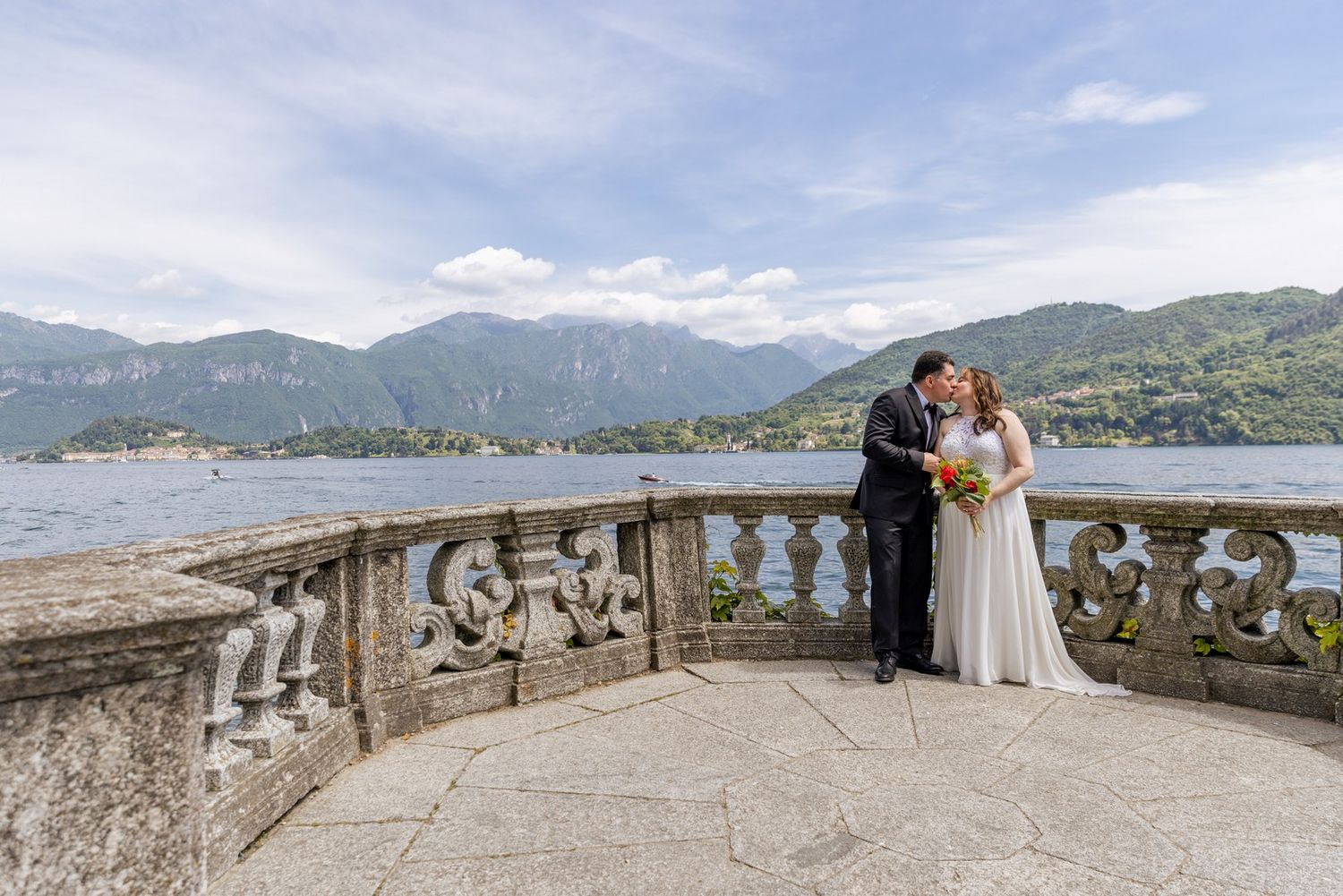 Panoramic view of a stone terrace overlooking a mountain lake with boats in the distance.