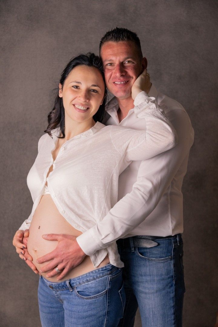 Maternity portrait of couple in white shirts against dark background.