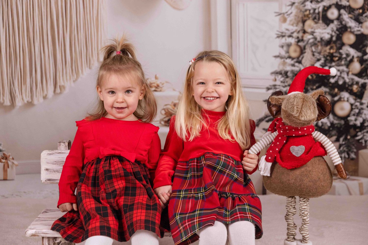 Children in festive red and plaid outfits pose together near decorated Christmas tree.