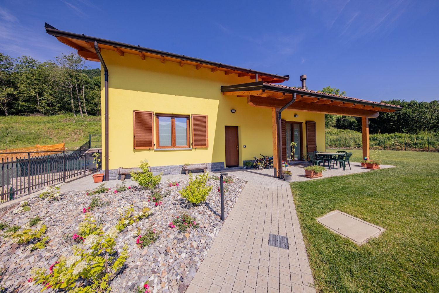 Yellow house with stone landscaping and covered porch in countryside setting.