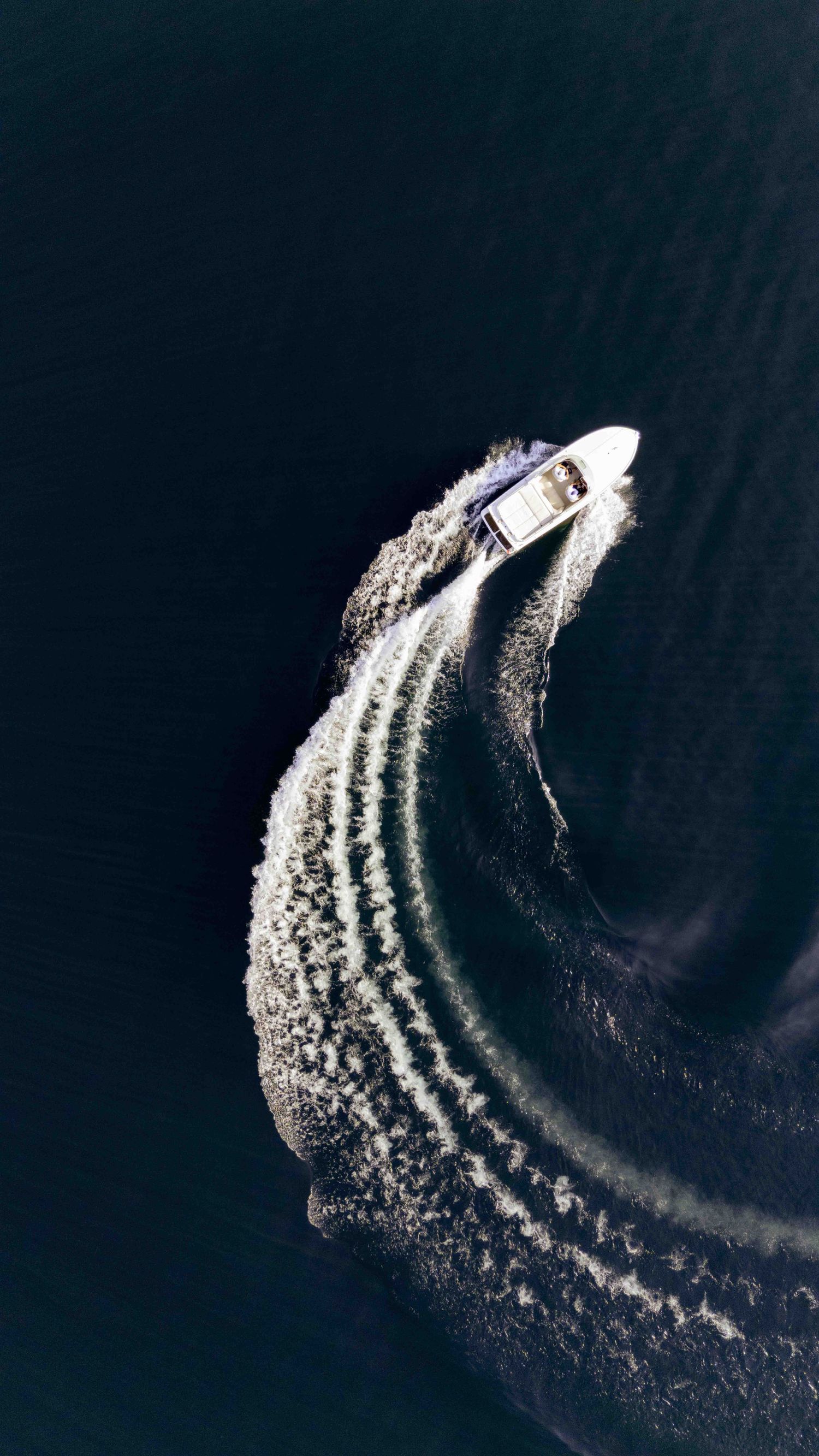Aerial view of speedboat creating dramatic wake patterns on dark waters.