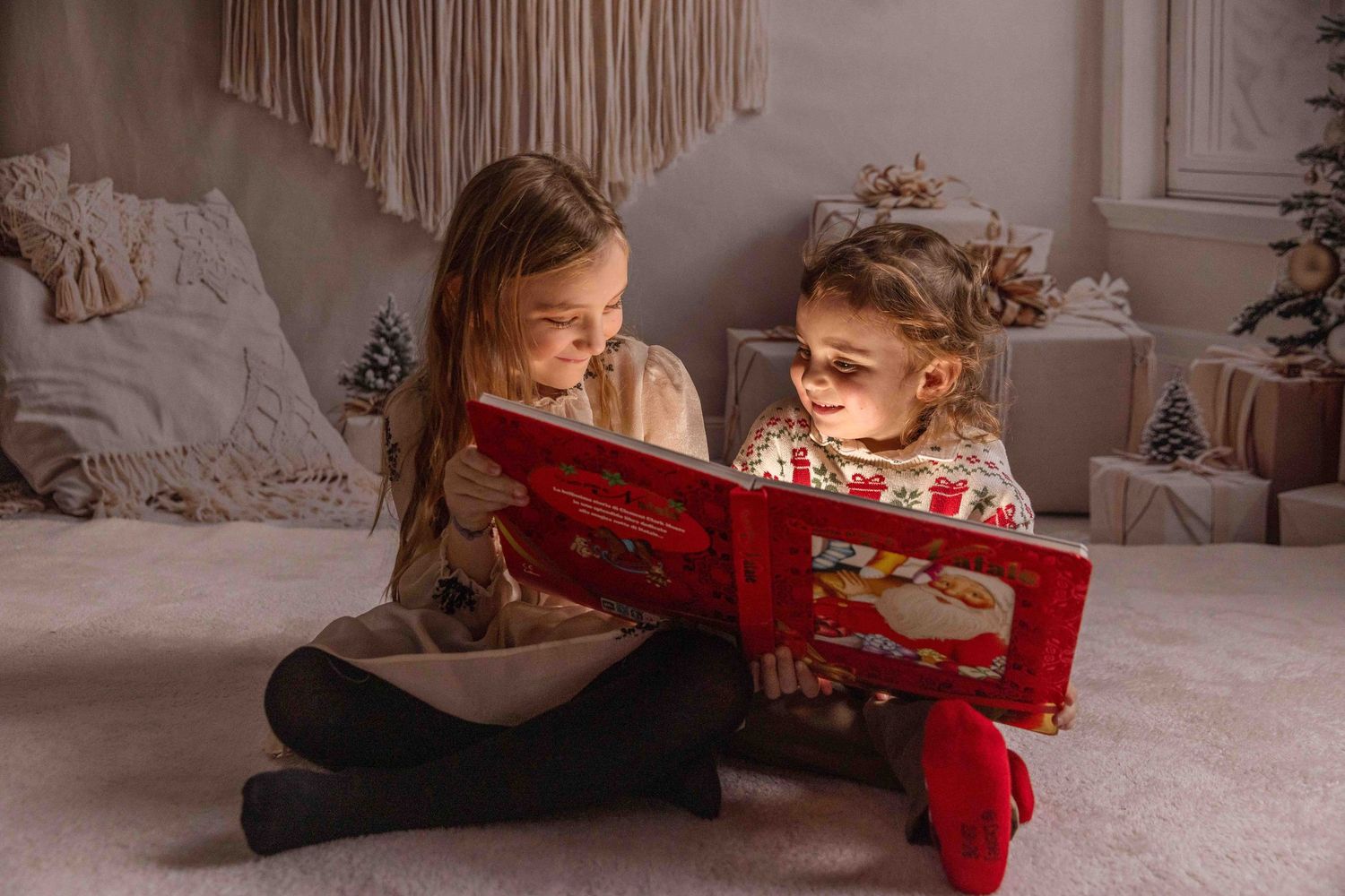 Child opening glowing red present box in cozy Christmas setting with macrame wall decor.