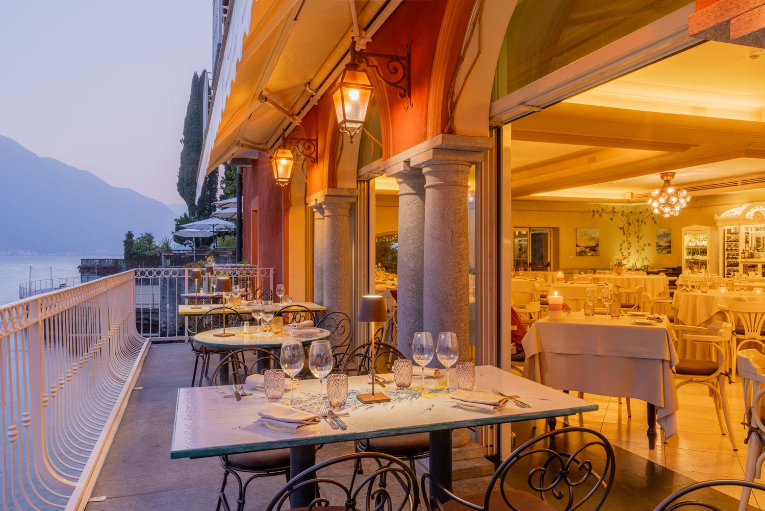Elegant lakeside restaurant terrace with mountain views and ambient lighting at dusk.