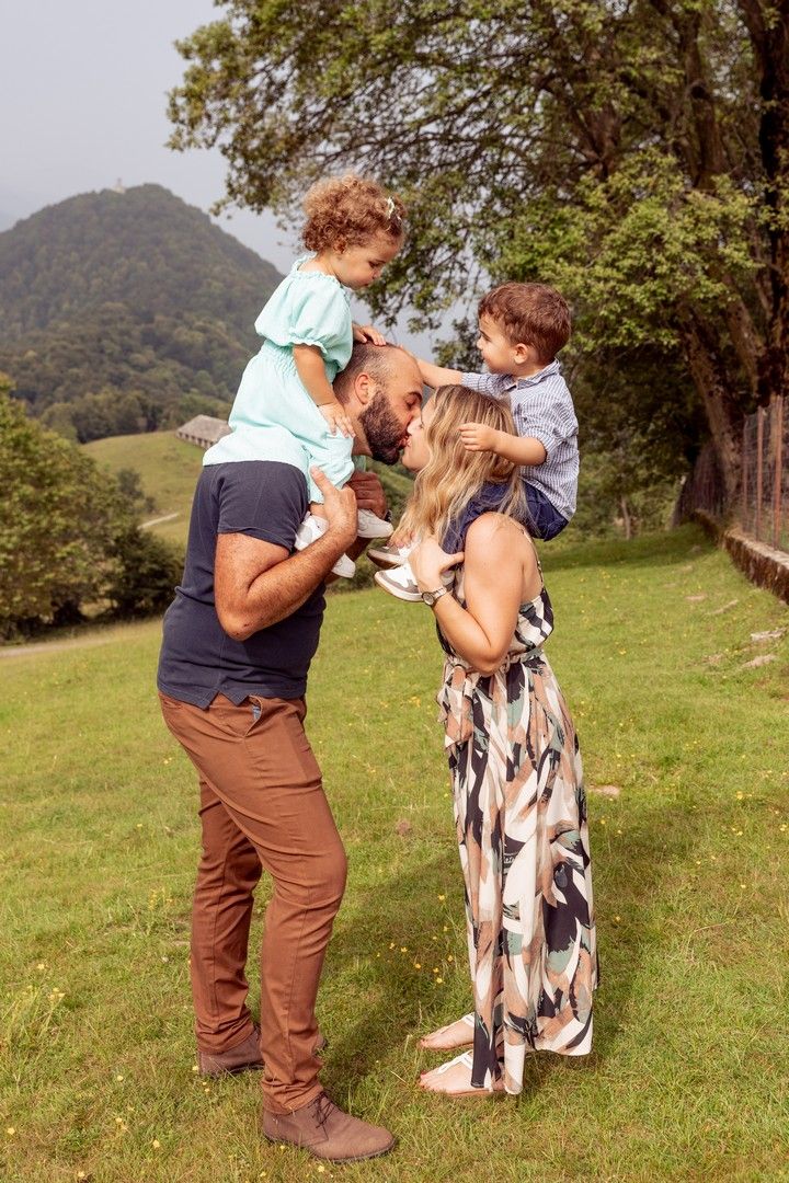 Family enjoying a playful moment together on a grassy hillside with mountains in the background.