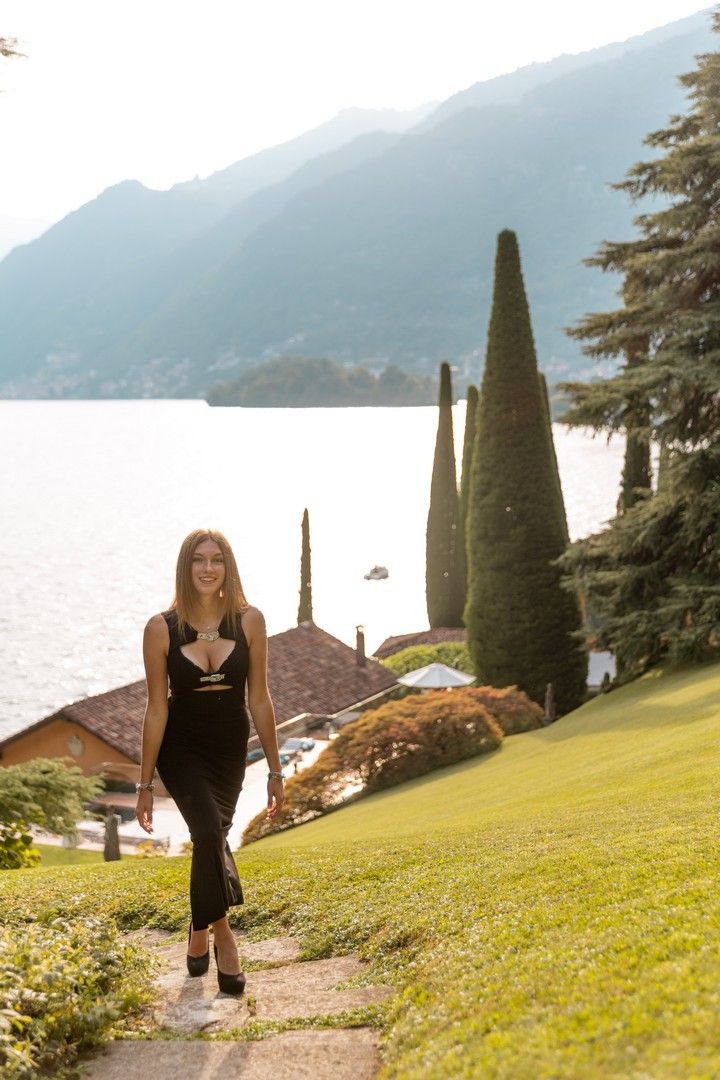 Person walking on grassy hillside with cypress trees and lake views.