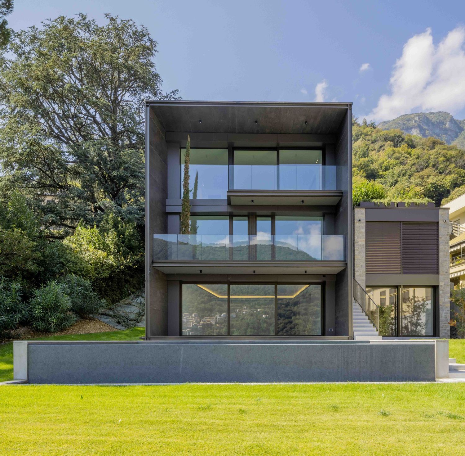 Sleek dark gray modern house with glass windows set on expansive green lawn.