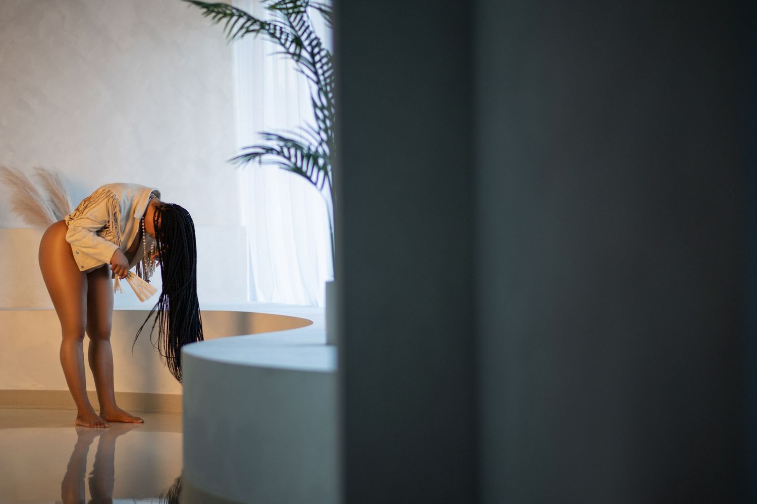 Woman leaning over a bathtub in a modern white bathroom with a plant in the background.