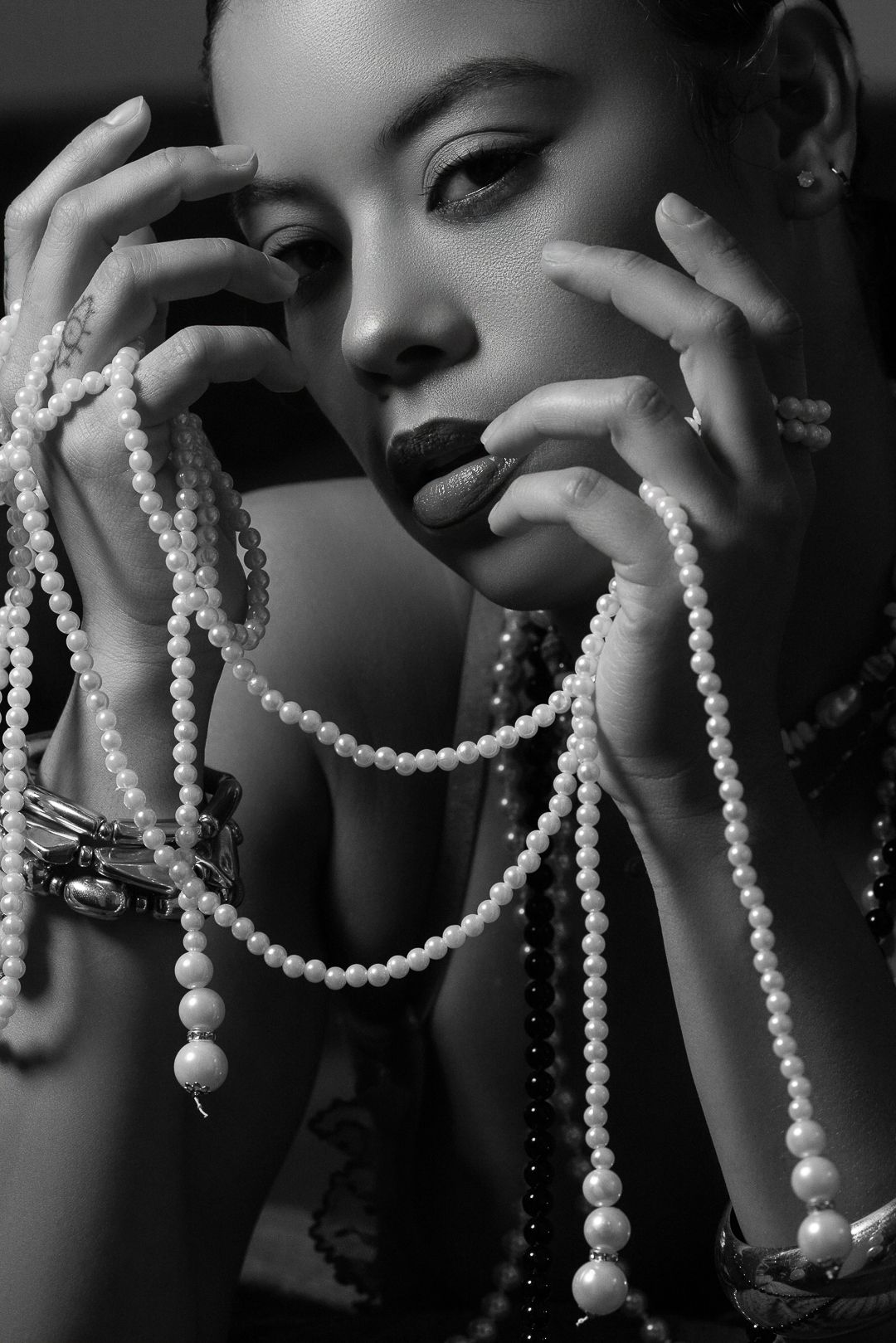 Dramatic close-up of pearl necklaces draped elegantly in black and white photography.