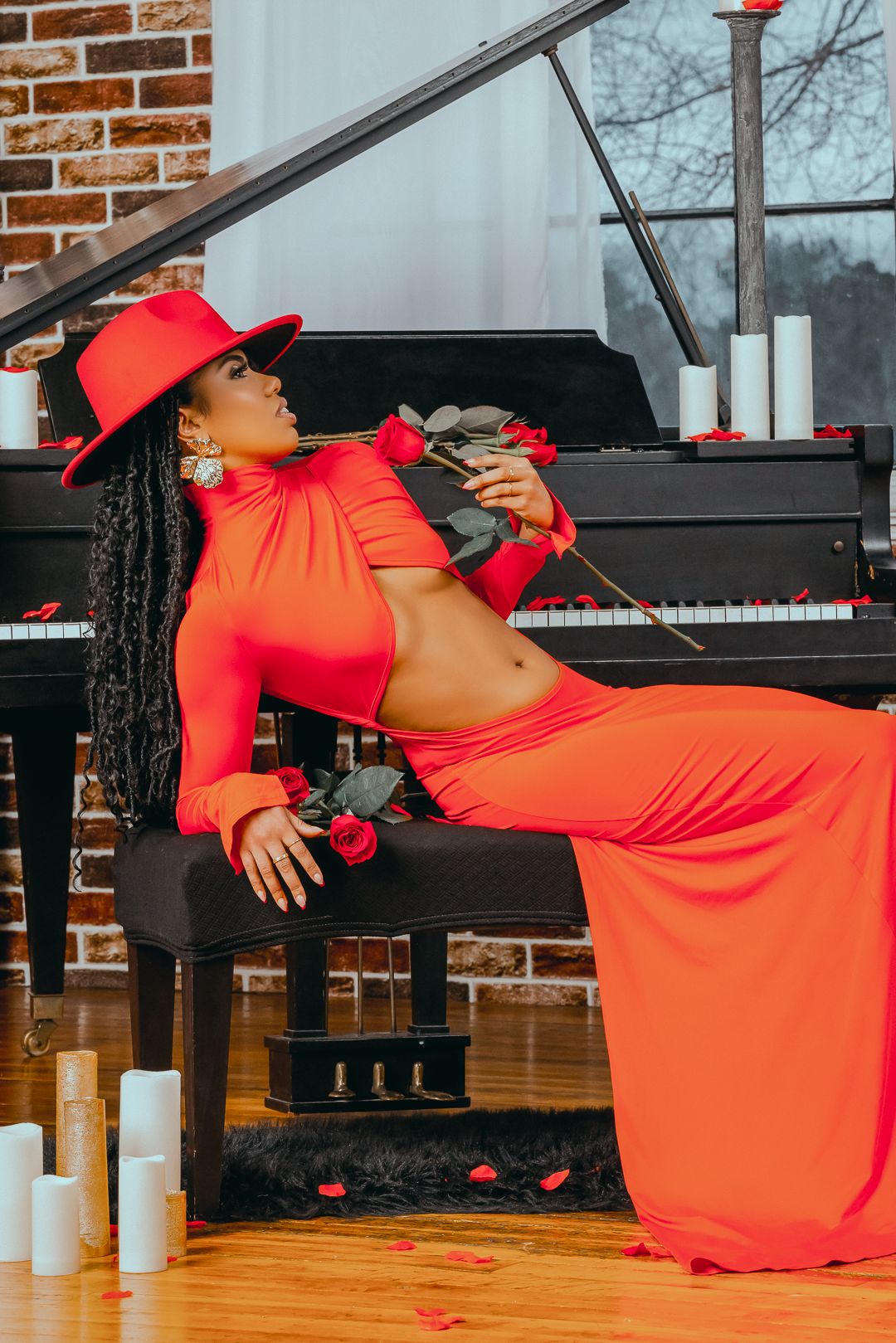 Dancer in bright orange dress performs dramatic floor choreography next to a grand piano in a studio setting.
