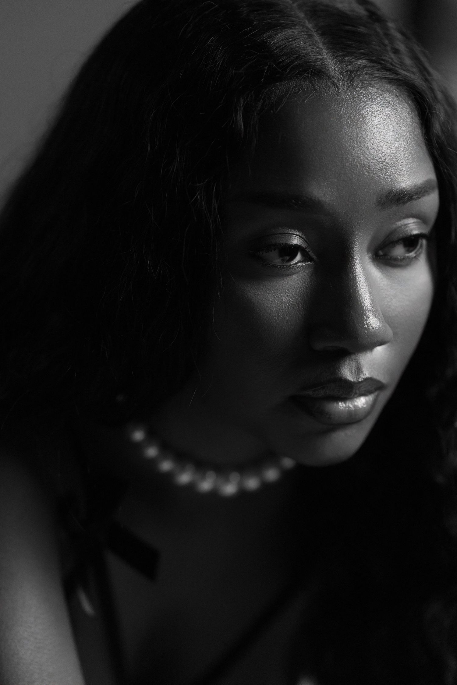 A dramatic black and white portrait series showing a person wearing pearls in moody lighting with various poses and expressions.