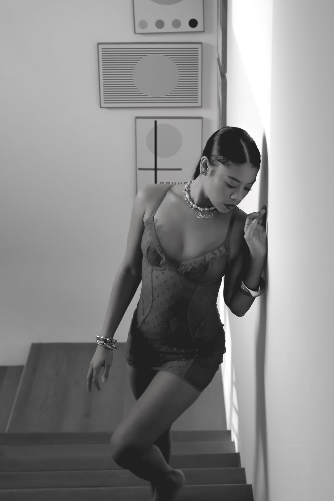 Black and white photo of a woman in a lace bodysuit leaning against a wall on a staircase.