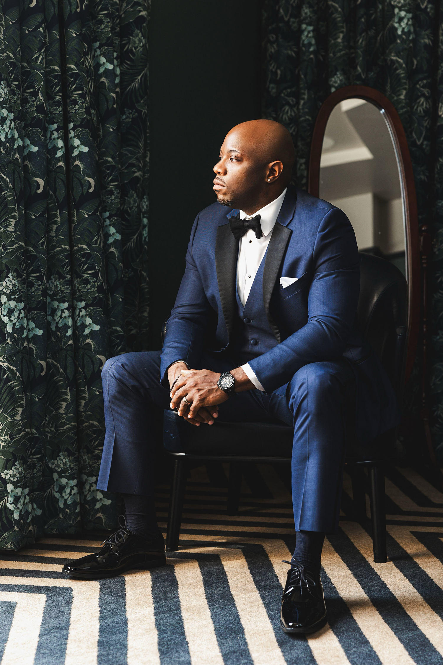 A collage of four photos showing a person in a navy blue suit sitting thoughtfully against a dark patterned background.