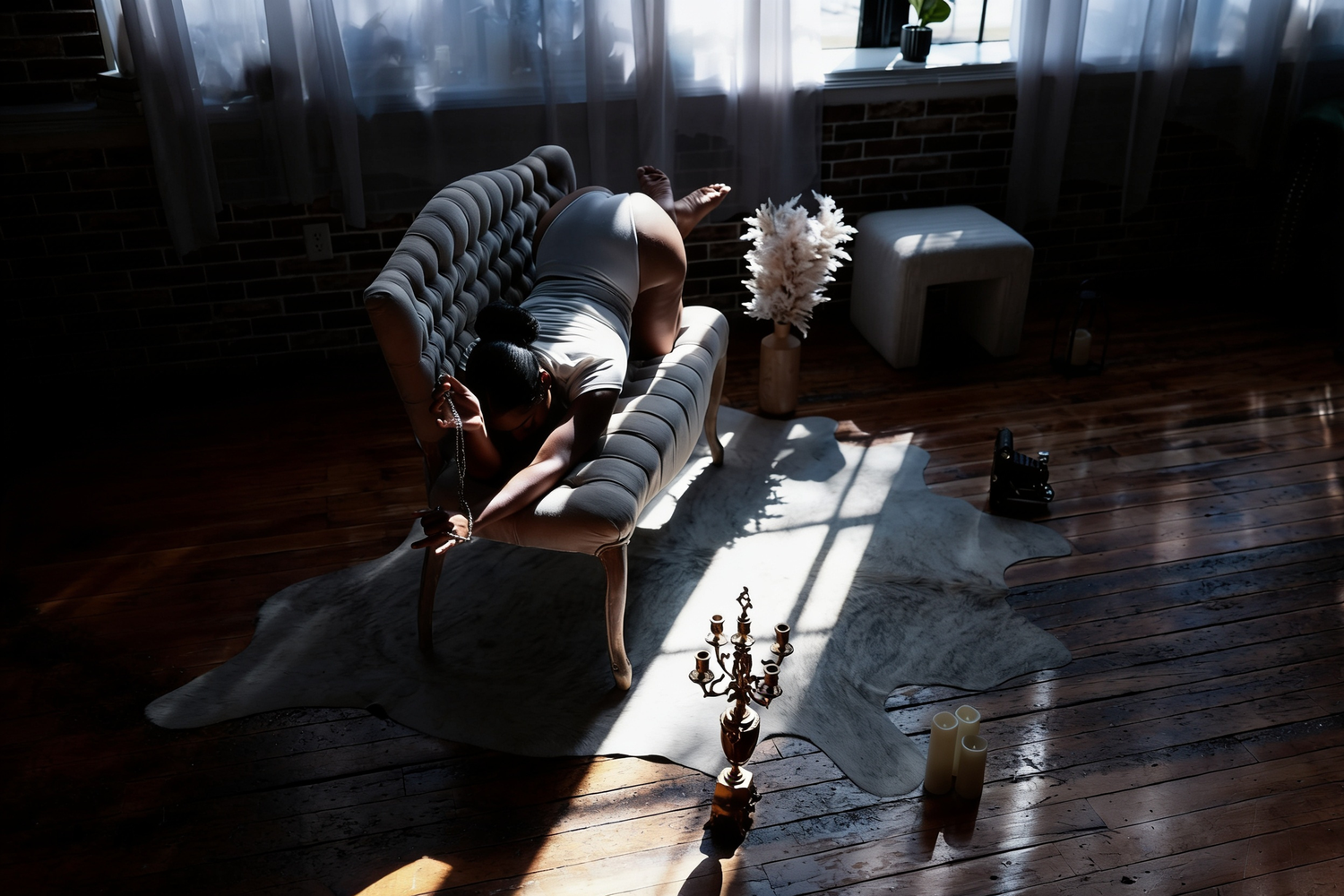 A person rests on a gray sofa in a sunlit room with hardwood floors, chess pieces, and sheer curtains.