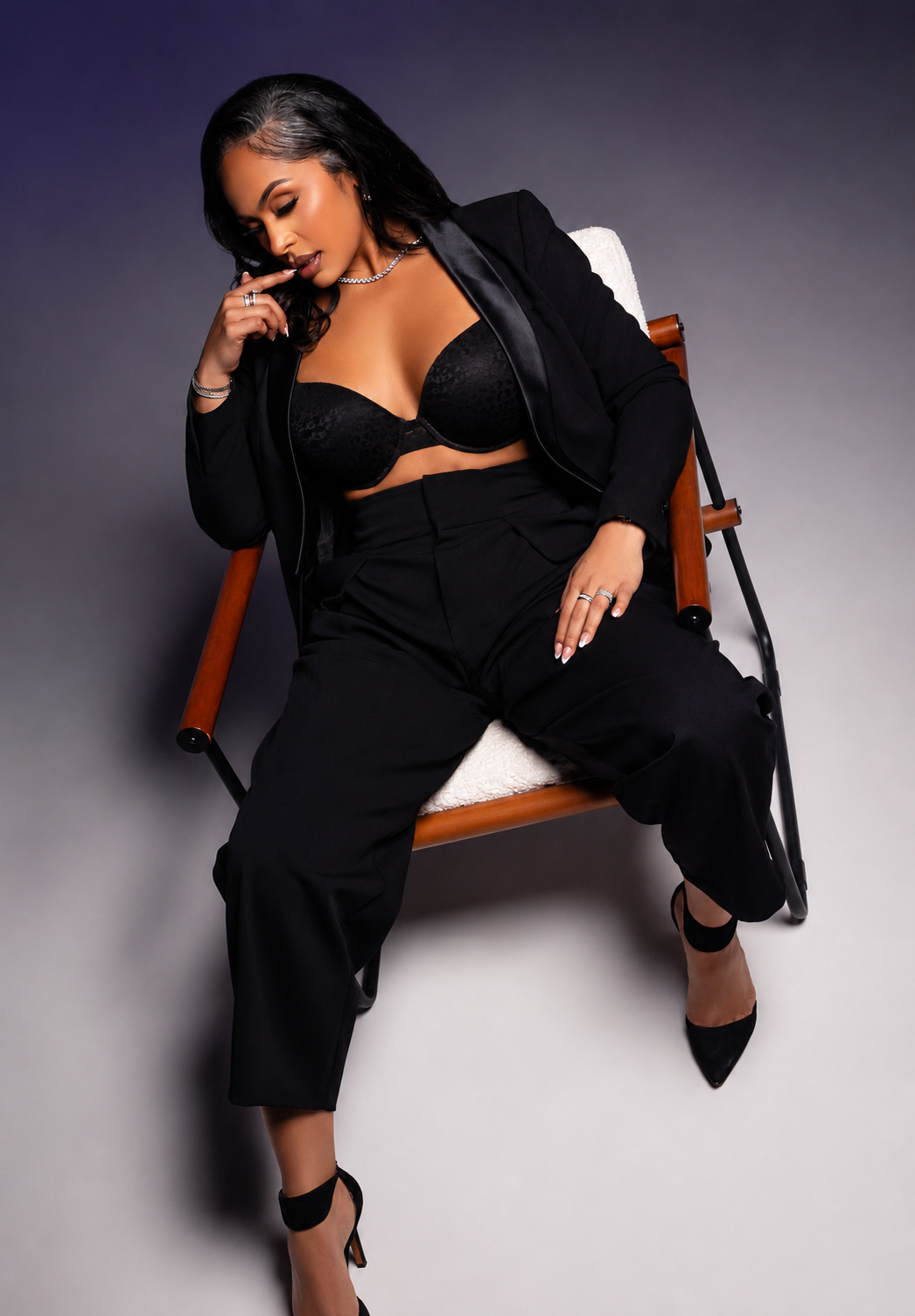 Woman in black blazer, bralette, and trousers poses confidently on a chair in a professional fashion photo.