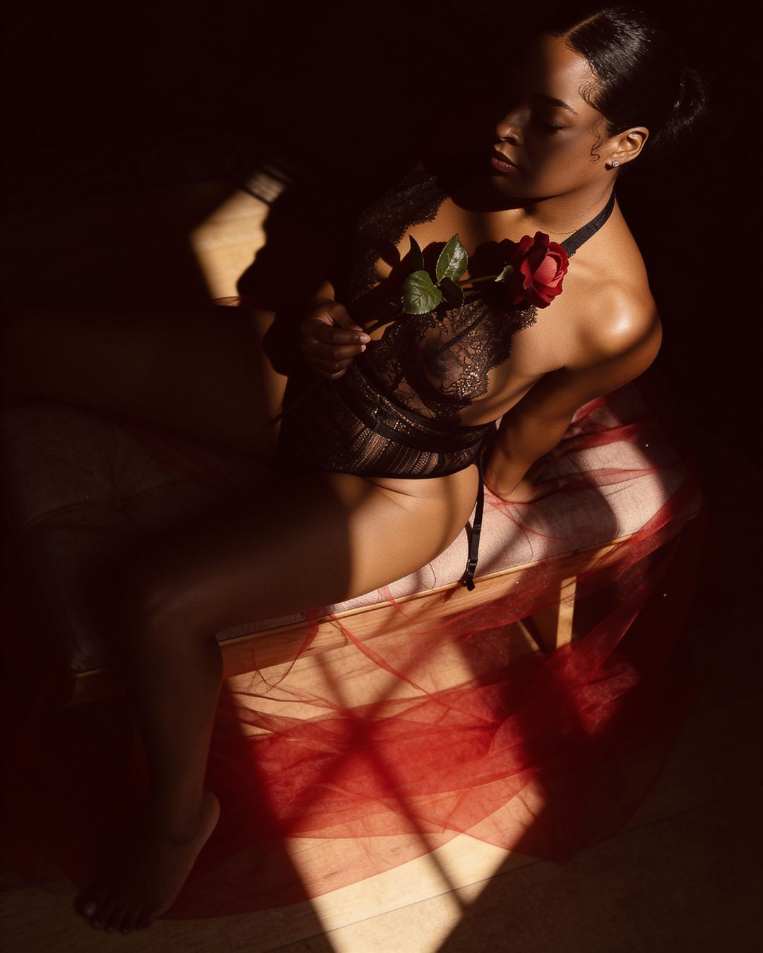 Woman in black lace lingerie holding a red rose, bathed in dramatic chiaroscuro lighting.