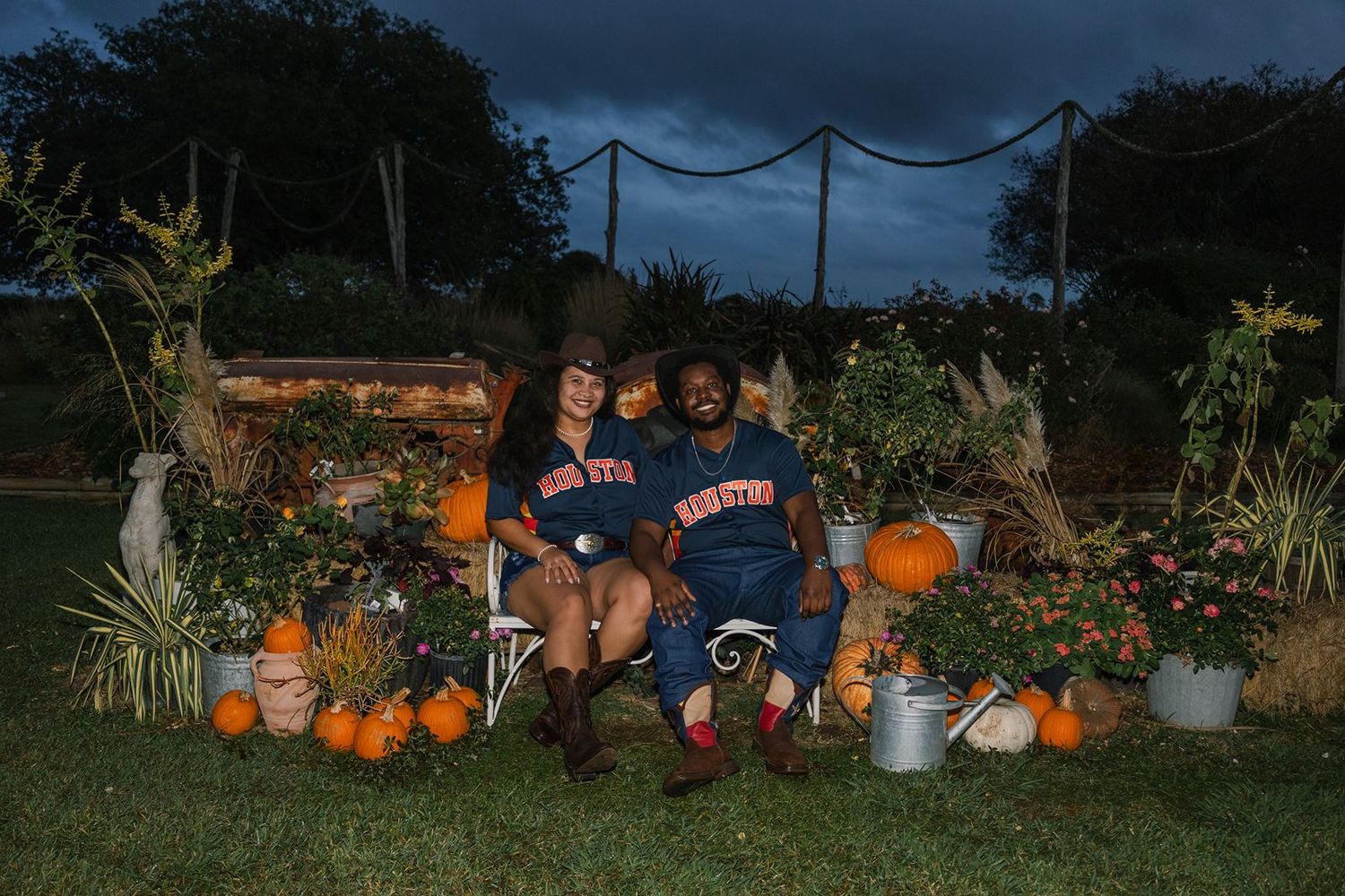 A festive fall display features carved pumpkins, cornstalks, and seasonal decorations along a dark walkway at dusk.