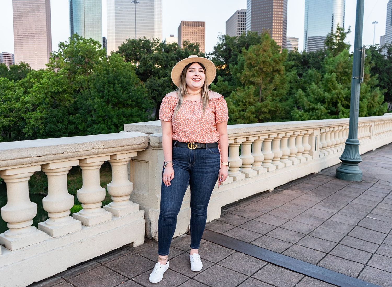 A person stands on a decorative balcony overlooking a city skyline with tall buildings and green trees visible.