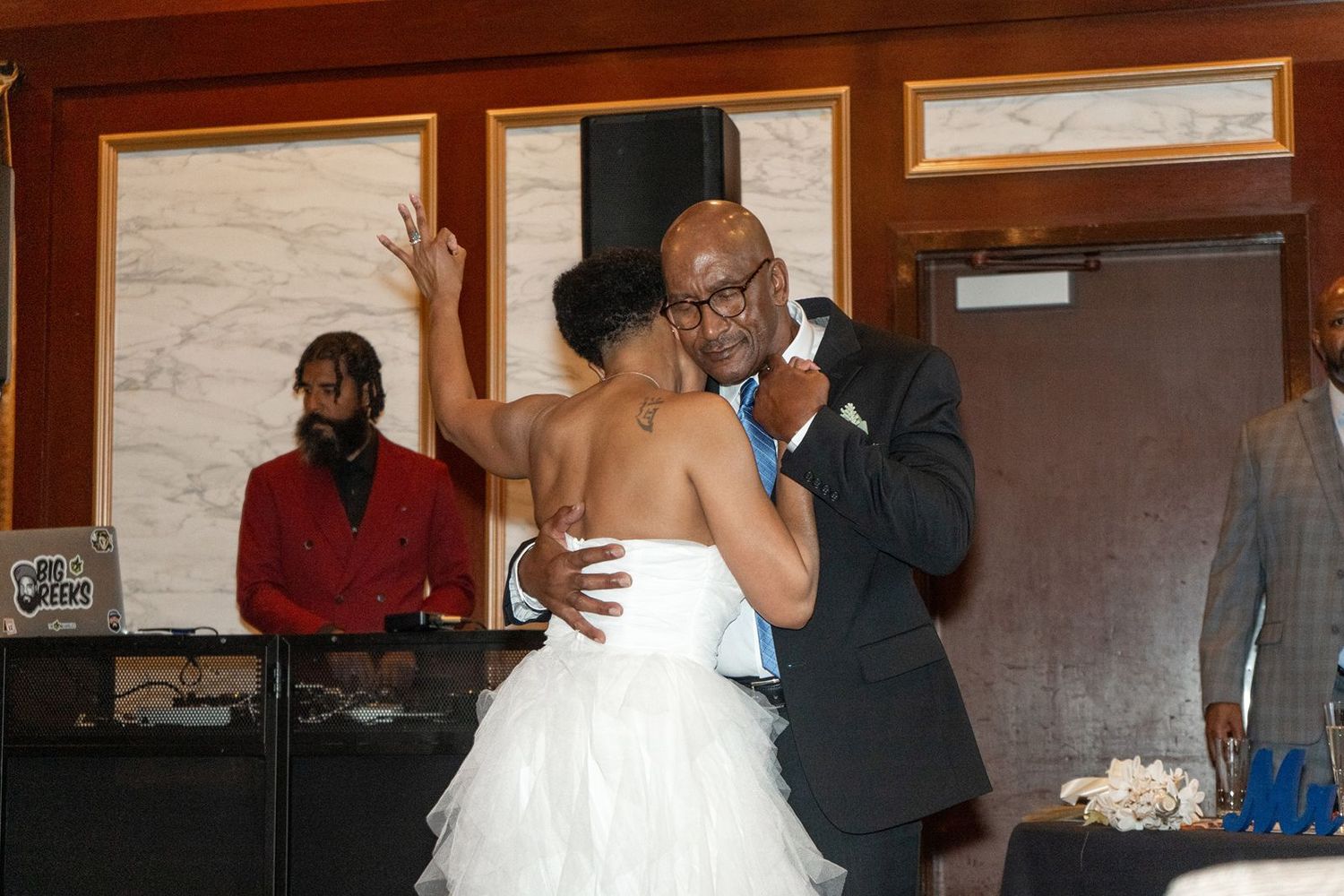 Bride and groom share first dance at wedding reception while DJ performs in background.
