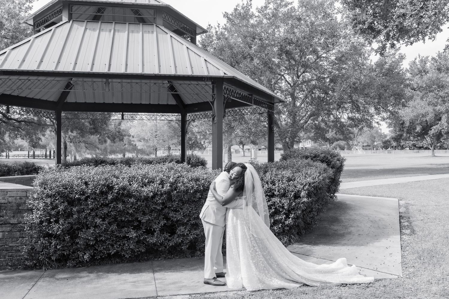 Black and white panorama of a park gazebo with metal roof surrounded by trees in a serene setting.