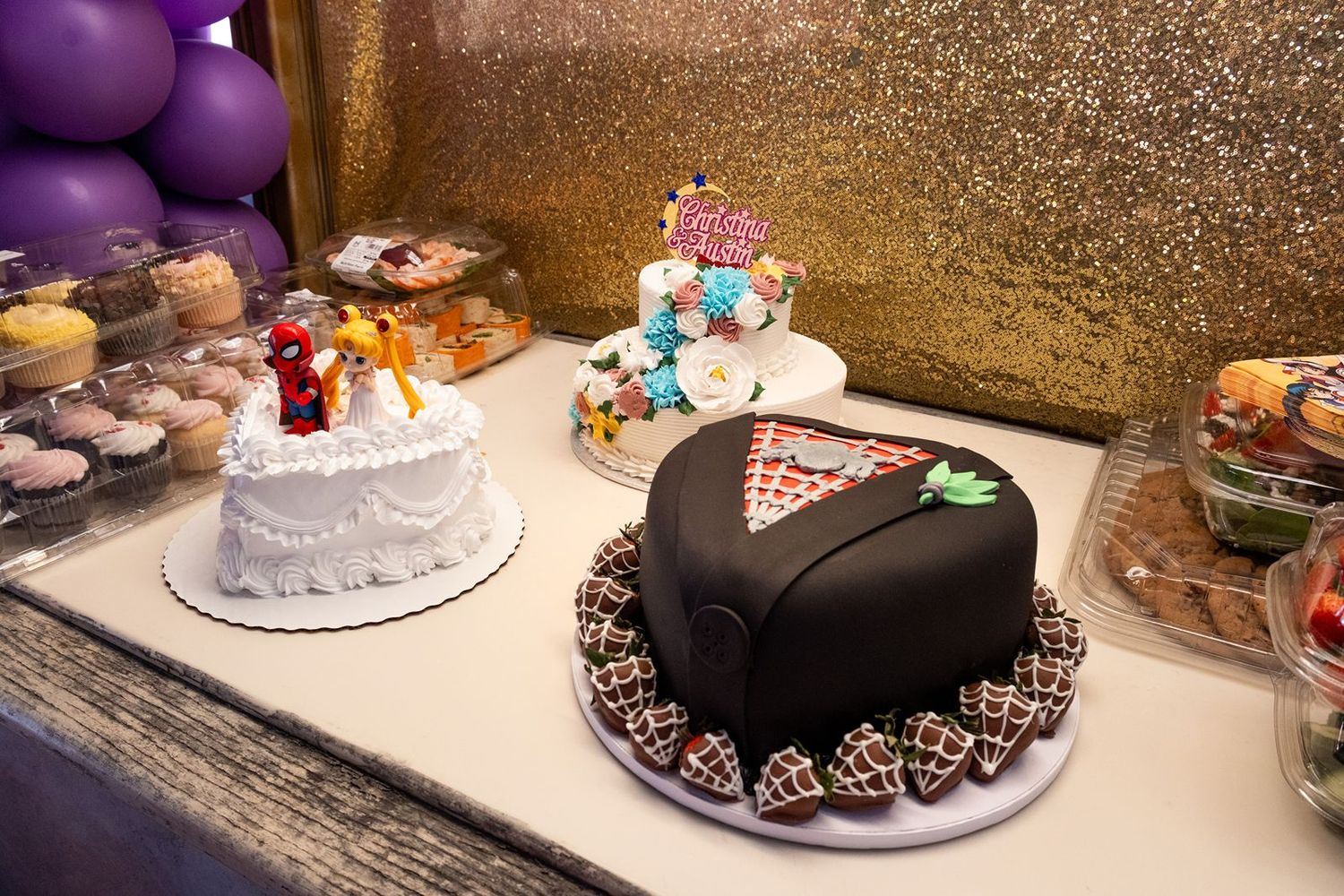 Colorful birthday party dessert table with decorated cakes, chocolate-covered strawberries, and purple balloons on a glittery backdrop.