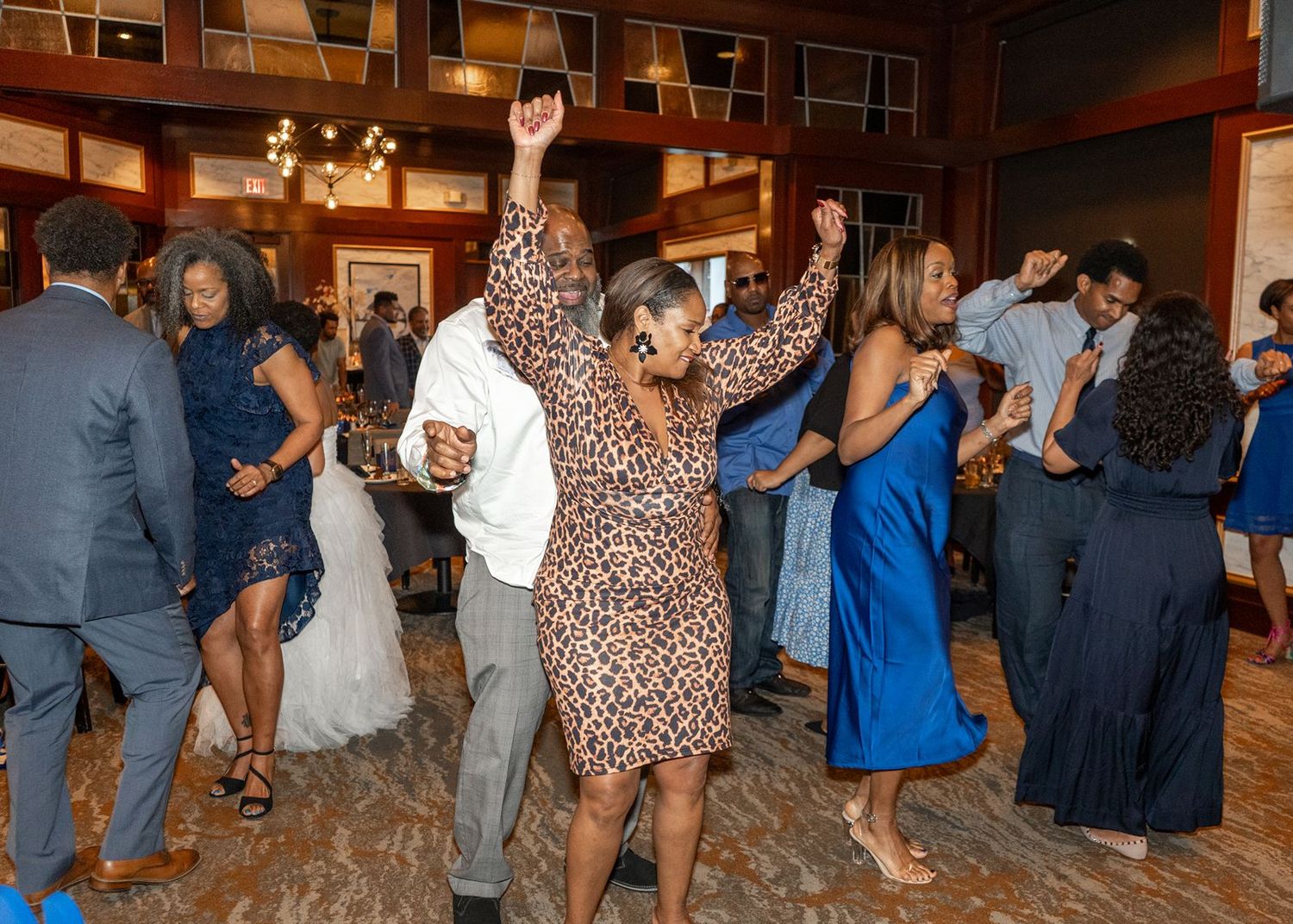 Wedding guests dancing together on a wooden dance floor at an indoor reception venue with warm lighting.