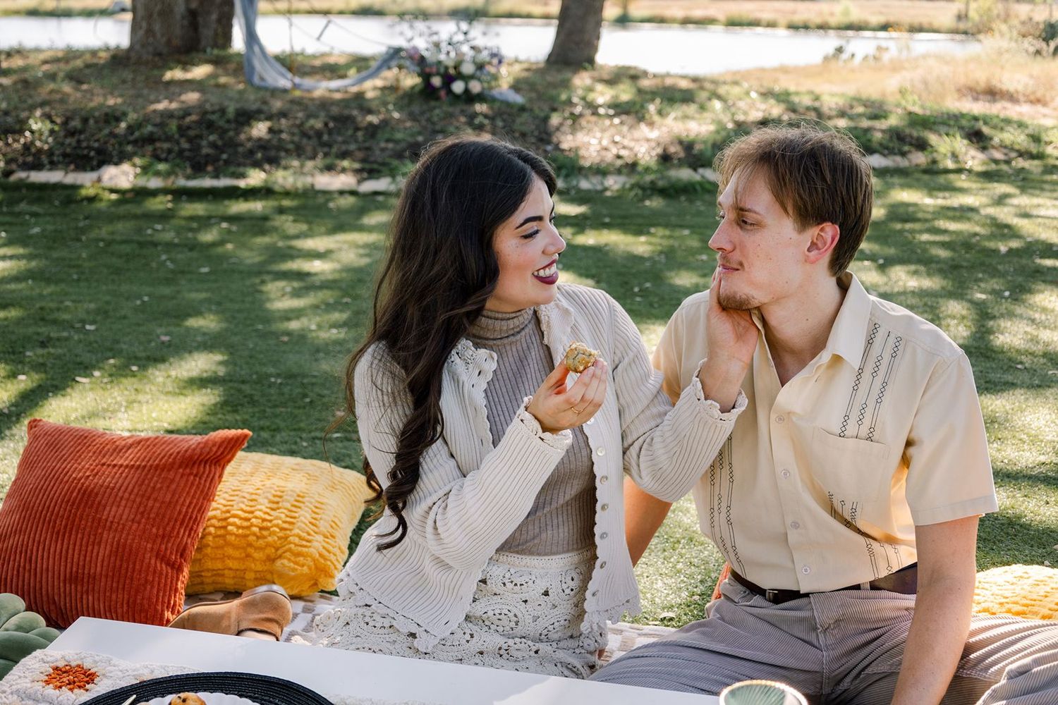 A couple shares a romantic moment during a sunny outdoor picnic in a grassy park setting.