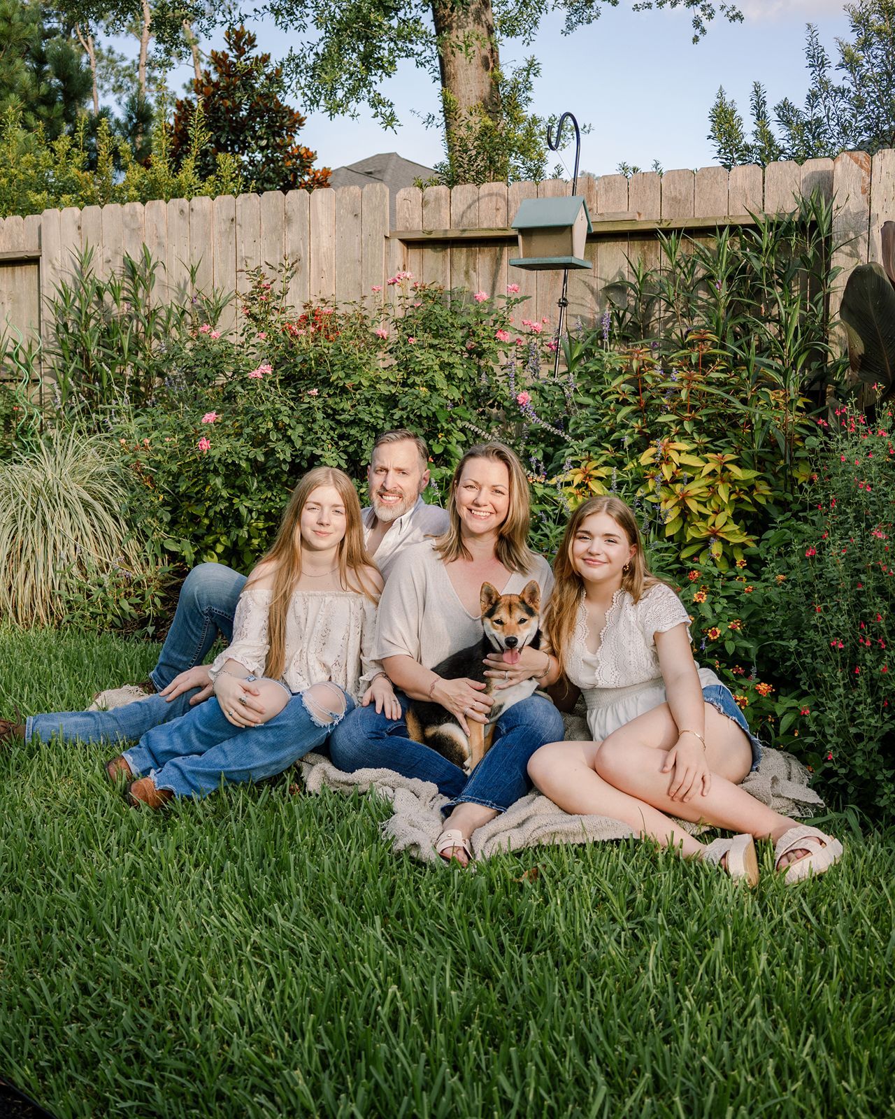 A group lounges together with their dog on lush green grass in a backyard garden setting.