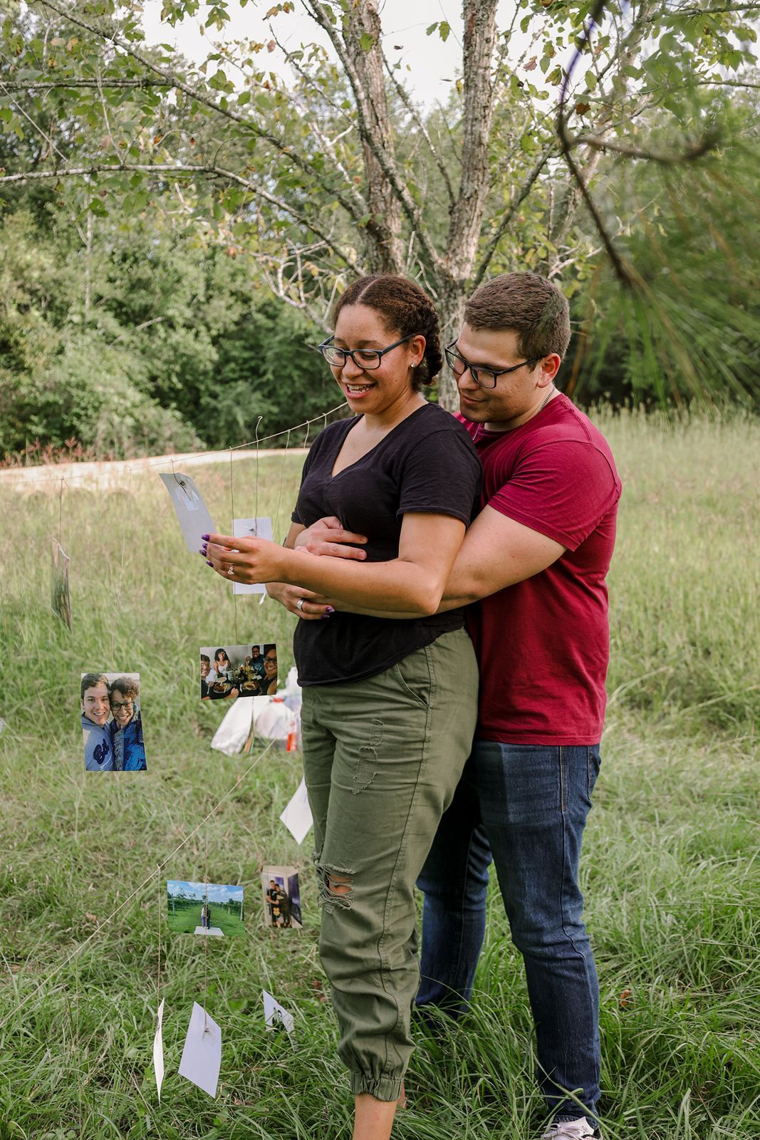 Couple reading a card together outdoors near a tree with photos displayed in a green field.